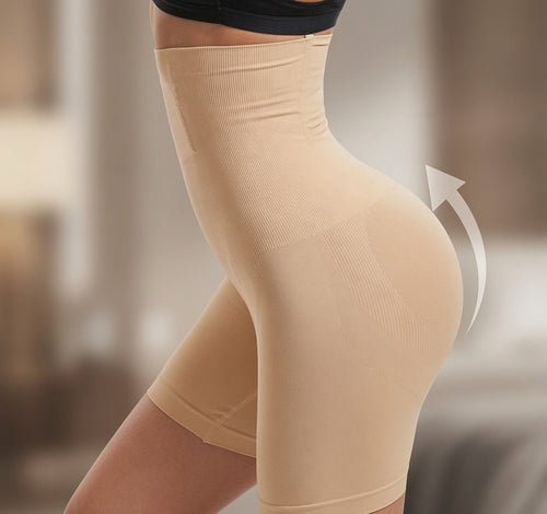 Close-up of a person wearing high-waisted beige shapewear shorts, with a white curved arrow graphic indicating shaping support. The background is softly blurred and neutral-toned.